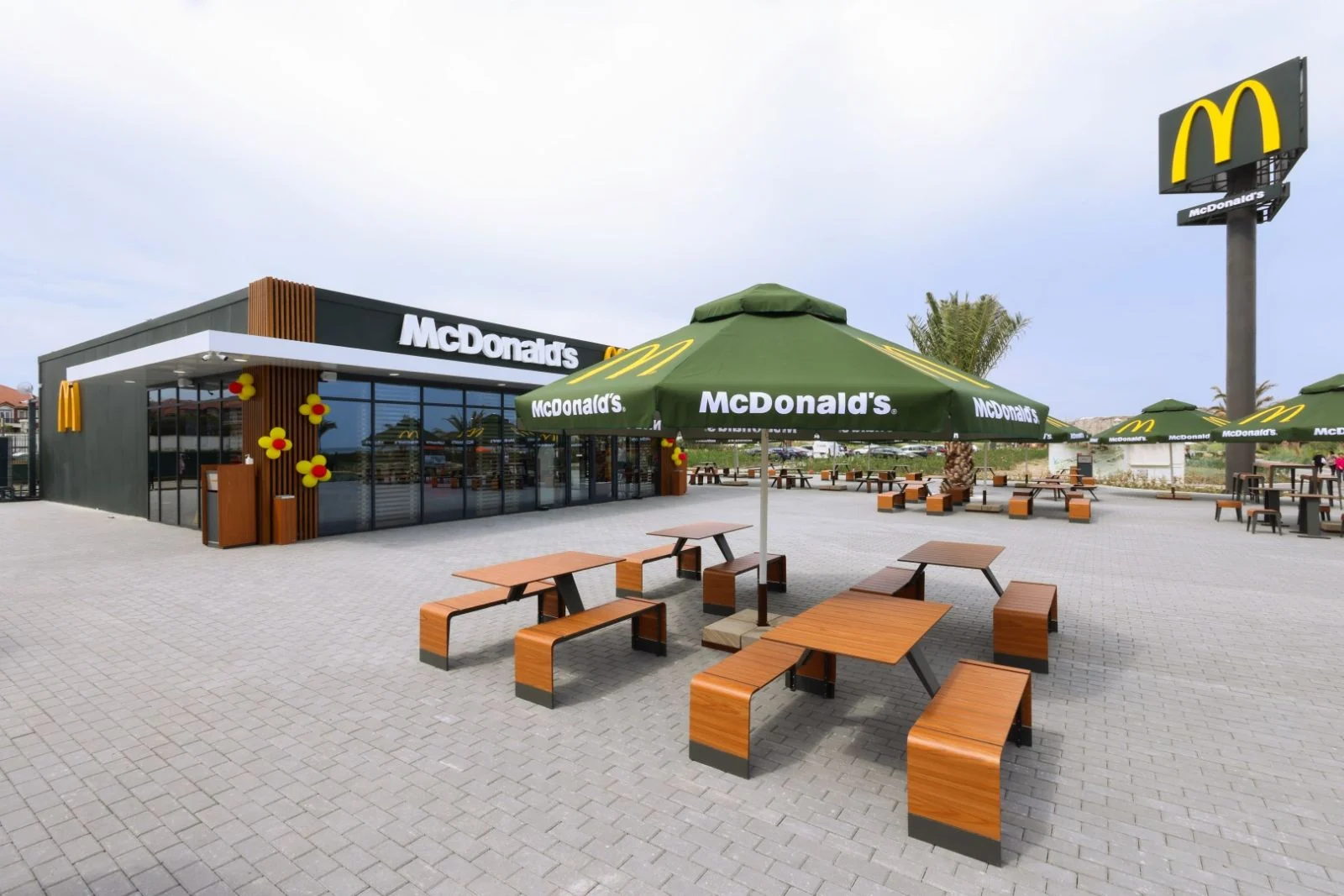 Терраса McDonald's Sea Breeze: столы и скамьи под зонтами, справа пилон с арками